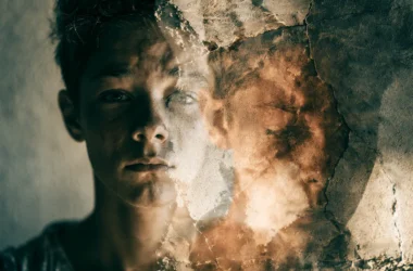 A conceptual double-exposure photo showing a young adolescent's face blended with a cracked, weathered wall texture, symbolizing political alienation and disillusionment. The left half reveals the youth's serious expression while the right dissolves into fractured, peeling surfaces, visually representing distrust, powerlessness, and psychological fragmentation associated with the pathway from system-disillusionment toward political radicalism in Swedish adolescents.