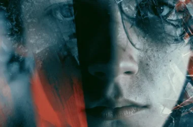 A photo showing a fragmented, close-up human face in muted blue-gray tones, overlaid with distorted textures and streaks of vivid red. The image is heavily manipulated with cracked, glass-like fractures and double-exposure effects that obscure the eyes, evoking themes of psychological rupture, obscured identity, and violence—visually paralleling the article's discussion of ideology-free extremism fixated on aggression itself.