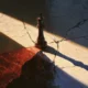 A conceptual painted illustration showing a solitary dark chess king piece standing on a cracked stone surface, casting a long shadow across a diagonal beam of light. Fractured lines radiate outward while a red glow pools at the base, symbolizing leadership, power orientation, and the destabilizing lethal influence of violent extremist organization leaders across their tenure.